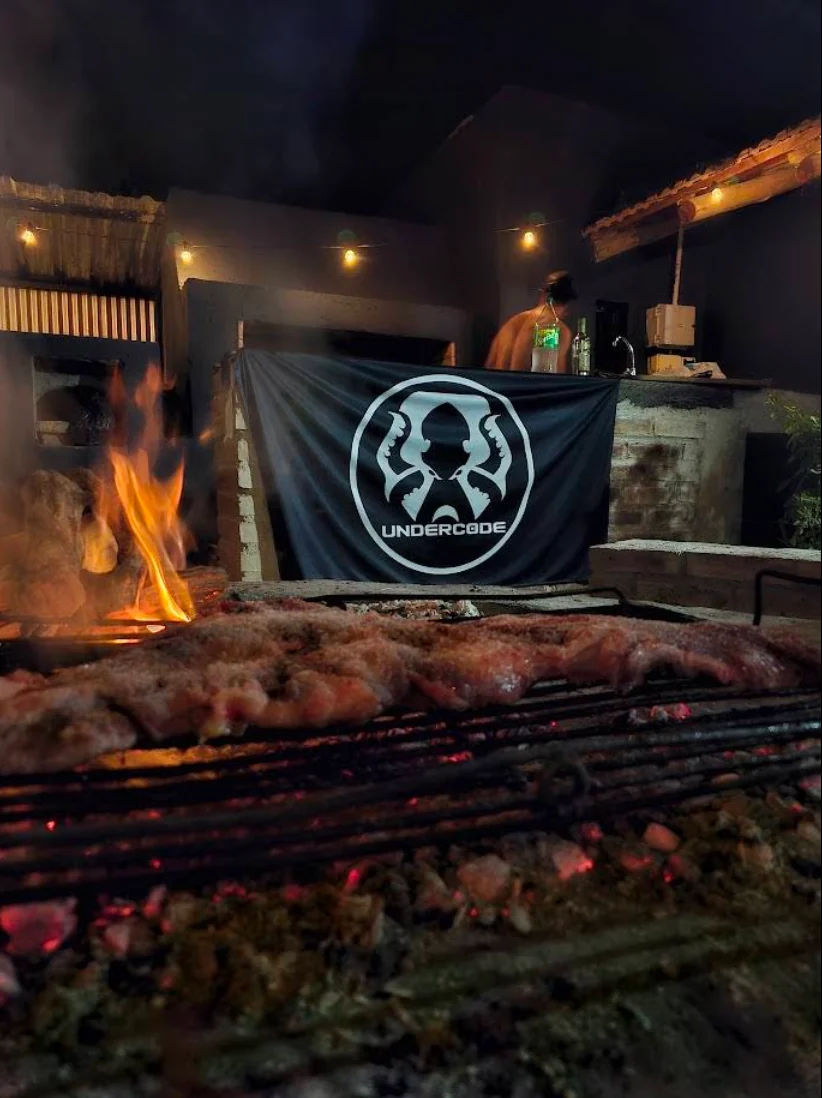Parrilla encendida con bandera de Underc0de al fondo